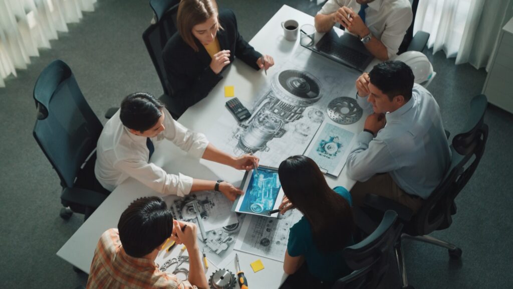 Team of engineers collaborating on innovative design project, reviewing blueprints and digital models.