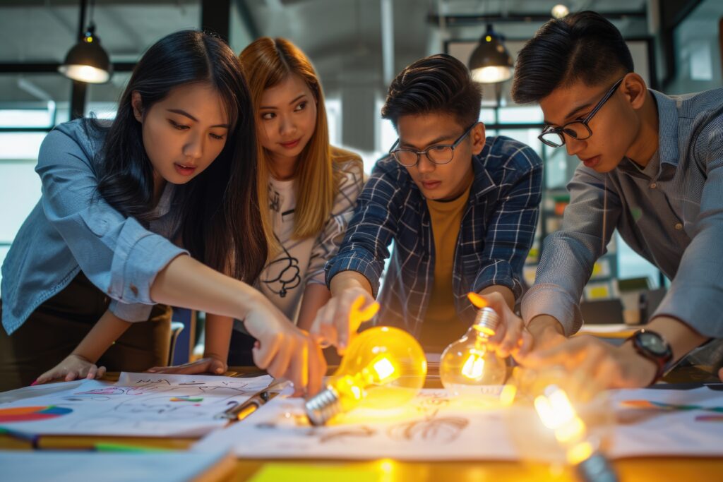 Four young professionals collaborate, holding illuminated lightbulbs, brainstorming ideas over project plans.