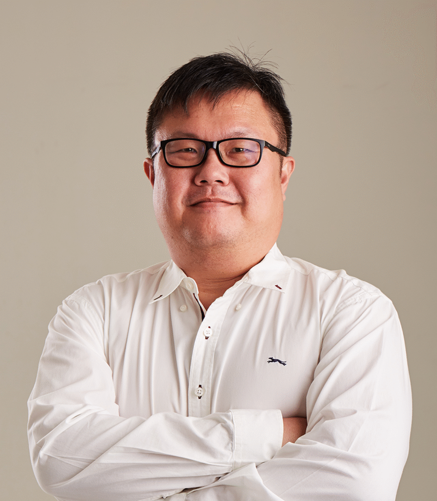 Portrait of a man wearing glasses and a white shirt, arms crossed.