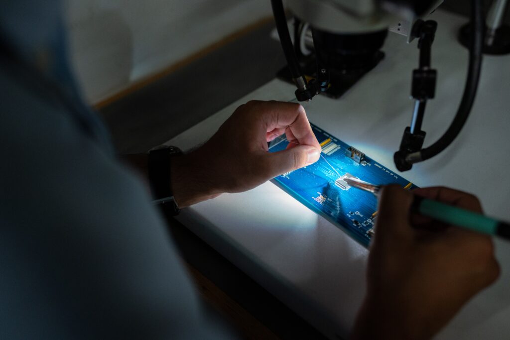 Close-up of hands soldering a circuit board under a microscope.