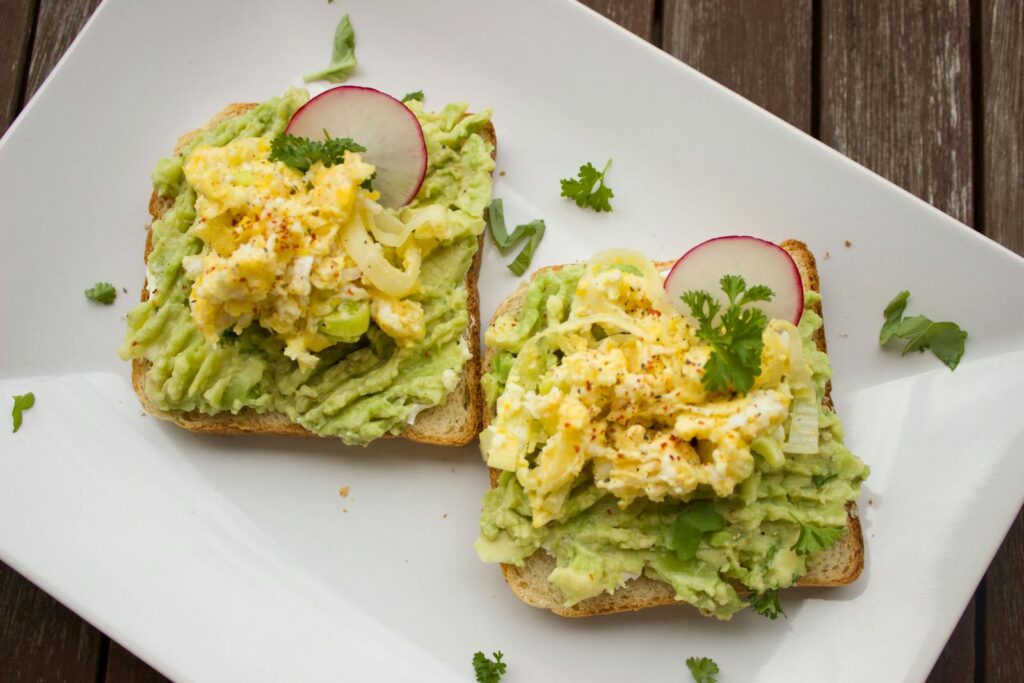 Deliciously prepared avocado and egg sandwiches garnished with radish on a white plate.